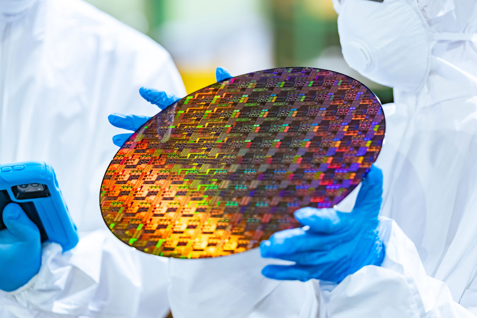 Technicians in cleanroom suits handling a semiconductor wafer