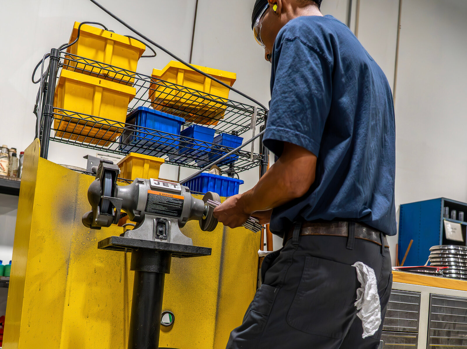 Technician finishing a machined part at a bench grinder in a Compass Precision facility
