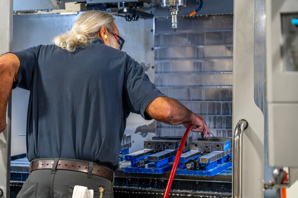 Machinist preparing vise fixtures inside a CNC vertical machining center at a Compass Precision facility