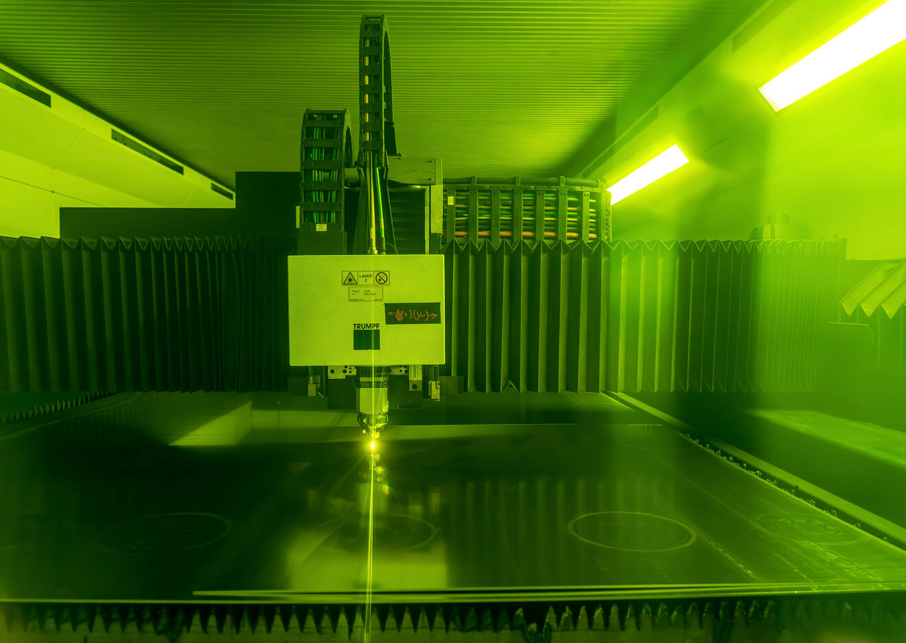Fiber laser cutting system processing sheet metal inside a green safety enclosure